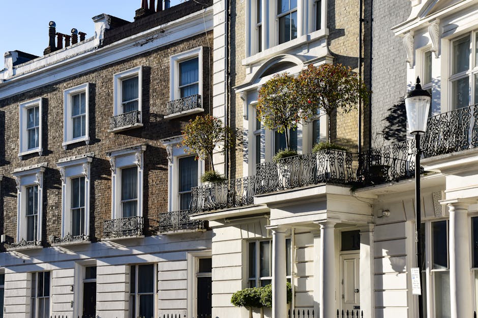 A row of three-story residential buildings with traditional London architecture, featuring brick facades on the upper levels and white painted or stone detailing on the lower levels. Each building has